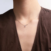 Person wearing a brown top with a necklace featuring a white zirconia against a neutral background